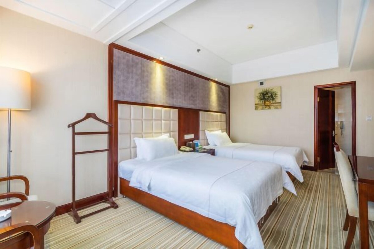 A hotel room with two beds, a desk, a chair, a lamp, and a painting on the wall.
