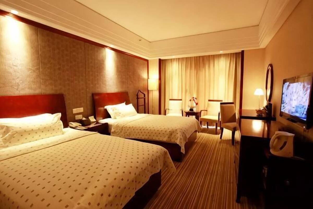 Habitación de hotel con dos camas, un escritorio con una silla, un televisor y una ventana con cortinas.