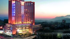 A high-rise hotel with multiple floors, a prominent entrance, and a view of surrounding buildings and mountains.