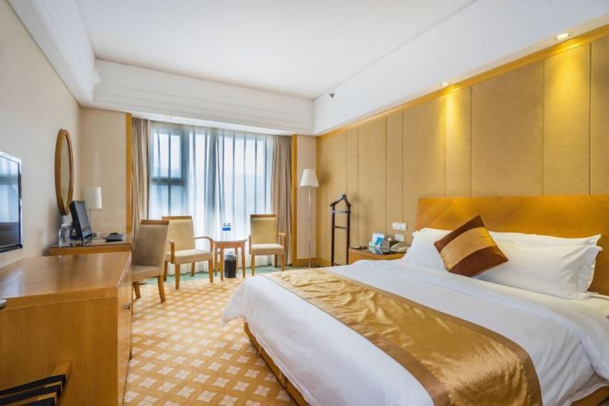 A hotel room with a large bed, a desk, a chair, and a television.
