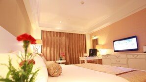 A hotel room with a large bed, a desk, a television, and a curtain.