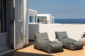 Un balcon avec deux fauteuils de jardin verts, un bâtiment blanc avec des volets bleus en arrière-plan et une vue sur la mer.