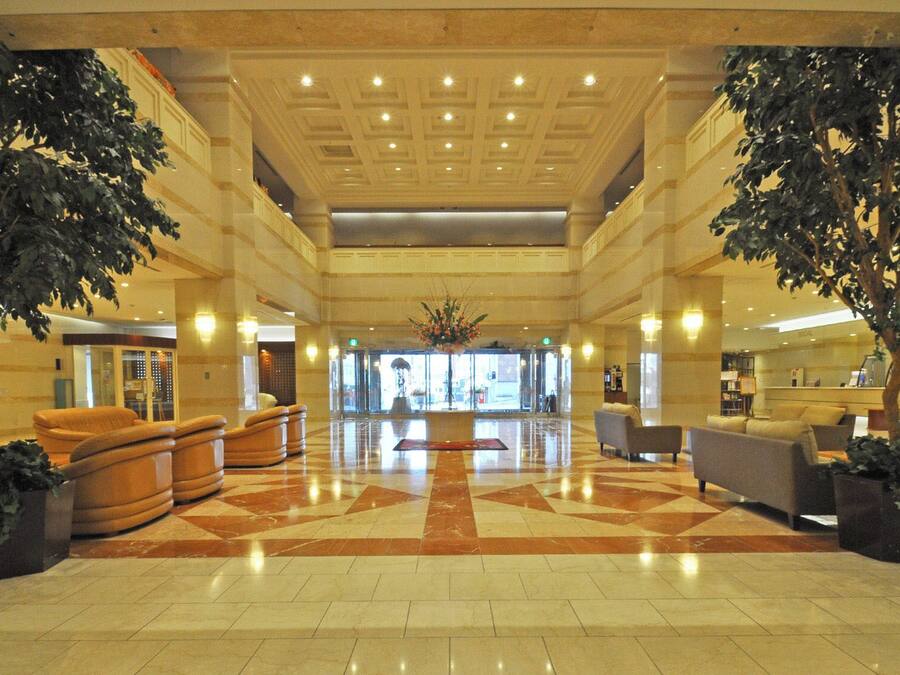 A spacious lobby with a checkered floor, large potted plants, and seating areas.