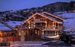 A wooden chalet with balconies and string lights, surrounded by snow-covered houses. - CHALET DE LUXE in MERIBEL, 18 pers - swimming pool - services included (Les Allues)