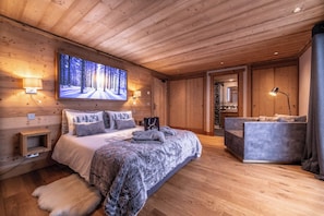 A cozy wooden cabin bedroom with a large bed, a sofa, and a wall-mounted TV. - CHALET DE LUXE in MERIBEL, 18 pers - swimming pool - services included (Les Allues)