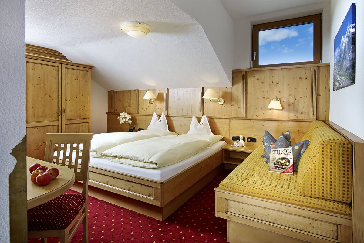 A hotel room with a wooden bed, a wooden desk, and a wooden chair. There is a window with a view of the sky and a painting on the wall.