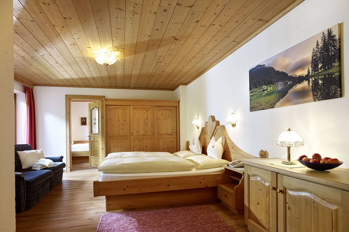 A wooden bedroom with a bed, bedside tables, a dresser, and a painting on the wall.