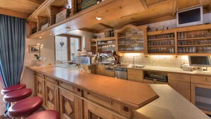 A kitchen with wooden cabinets, a countertop, and a bar area with stools. - Hotel Traube (Pettneu am Arlberg)