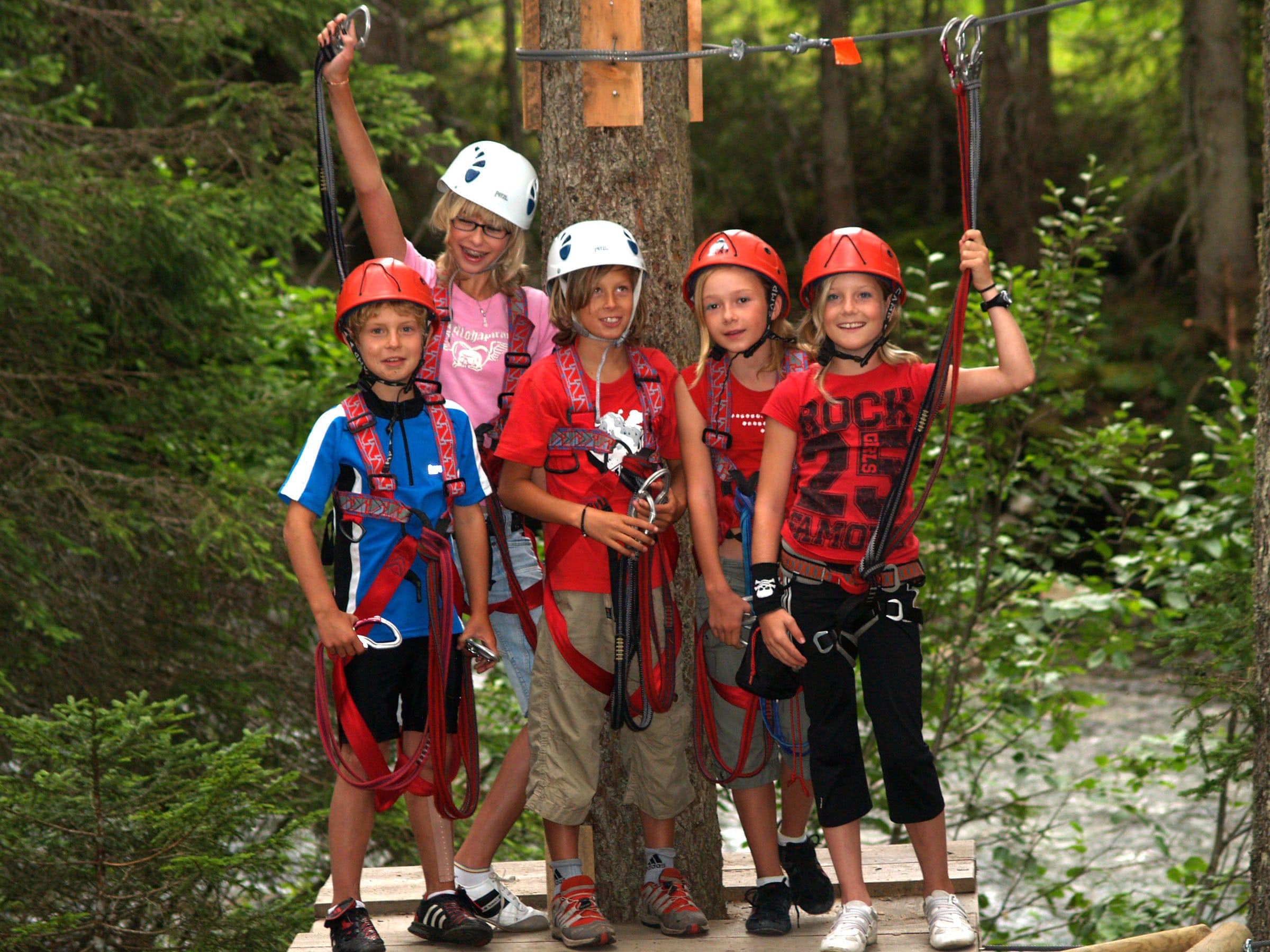Un grupo de niños disfrutando de una aventura en tirolesa, con cascos y arneses, en un área boscosa.
