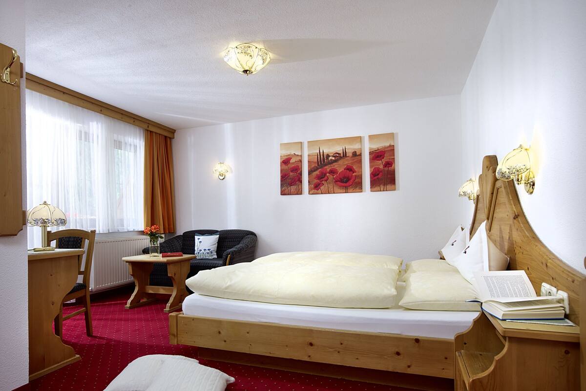 A hotel room with a wooden bed, a desk with a lamp, a chair, and a radiator.