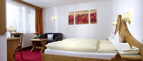 A hotel room with a wooden bed, a desk with a lamp, a chair, and a radiator.