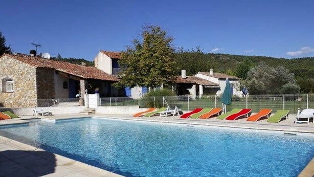 Una piscina con lettini, edifici in pietra e cielo sereno.