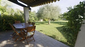 Un portico coperto con tavolo e sedie, circondato da un prato curato e alberi.