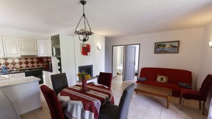 Zona pranzo con tavolo apparecchiato per quattro, circondato da sedie e un divano rosso sullo sfondo.