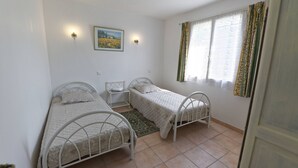 Una camera da letto con due letti singoli, un tavolino, una lampada da comodino, una luce fissata al muro, un quadro incorniciato e una finestra con tende.