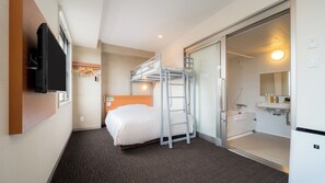 Habitación de hotel con literas, un televisor montado en la pared, un baño con lavamanos y espejo, y piso cubierto de alfombra.