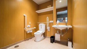 A modern bathroom with a toilet, bidet, and sink, equipped with accessibility features like grab bars and a handrail. - Super Hotel Kumamoto Yamaga (Yamaga)