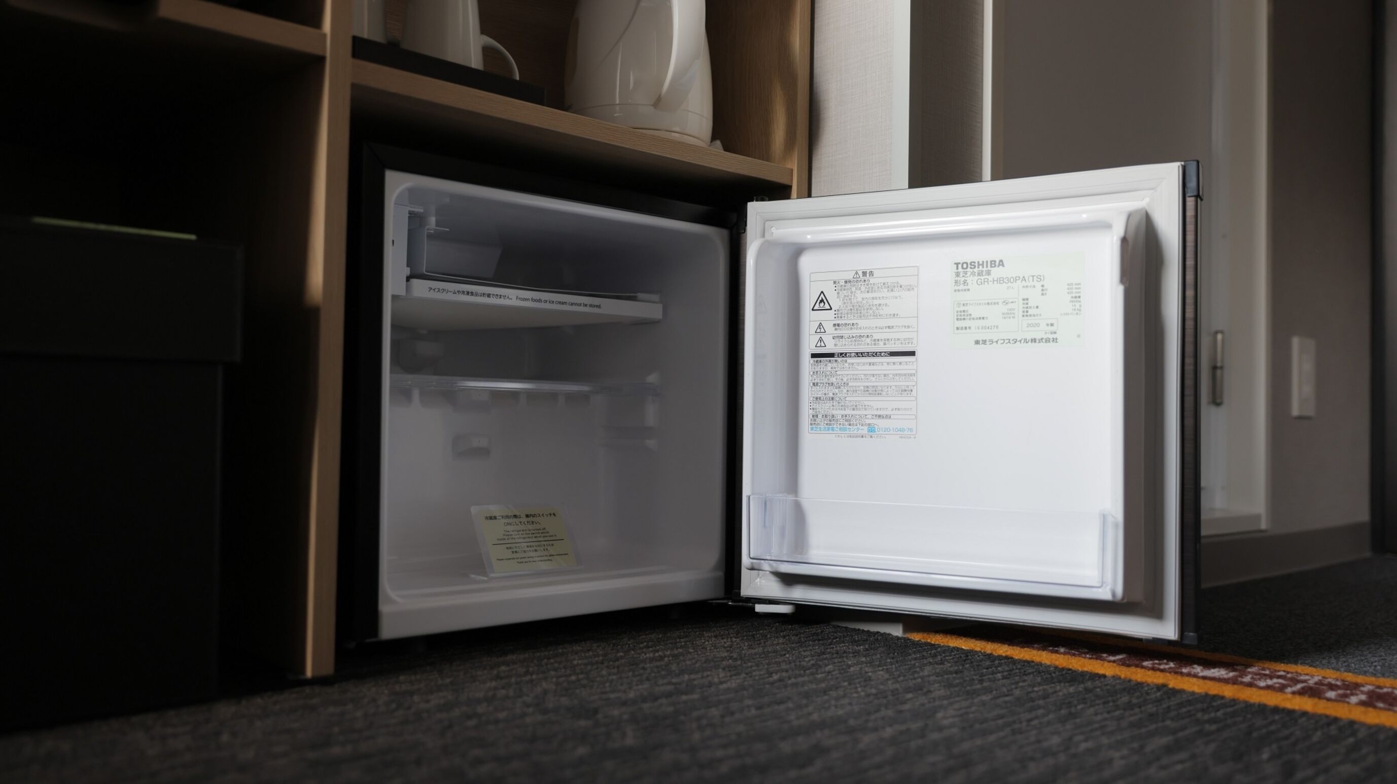 An open refrigerator with a control panel on the right side, a warning label on the left, and a shelf above the door.