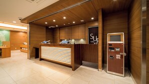 A hotel reception desk with a wooden finish, a digital check-in kiosk, and a self-service machine. - Super Hotel Kumamoto Yamaga (Yamaga)