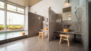 Ein modernes Badezimmer mit Granit-Arbeitsplatten, Holzschemeln, einem großen Spiegel und einer Duschkabine.