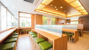 A modern restaurant interior with wooden tables and green stools, large windows, and a wooden ceiling with recessed lighting. - Super Hotel Kumamoto Yamaga (Yamaga)