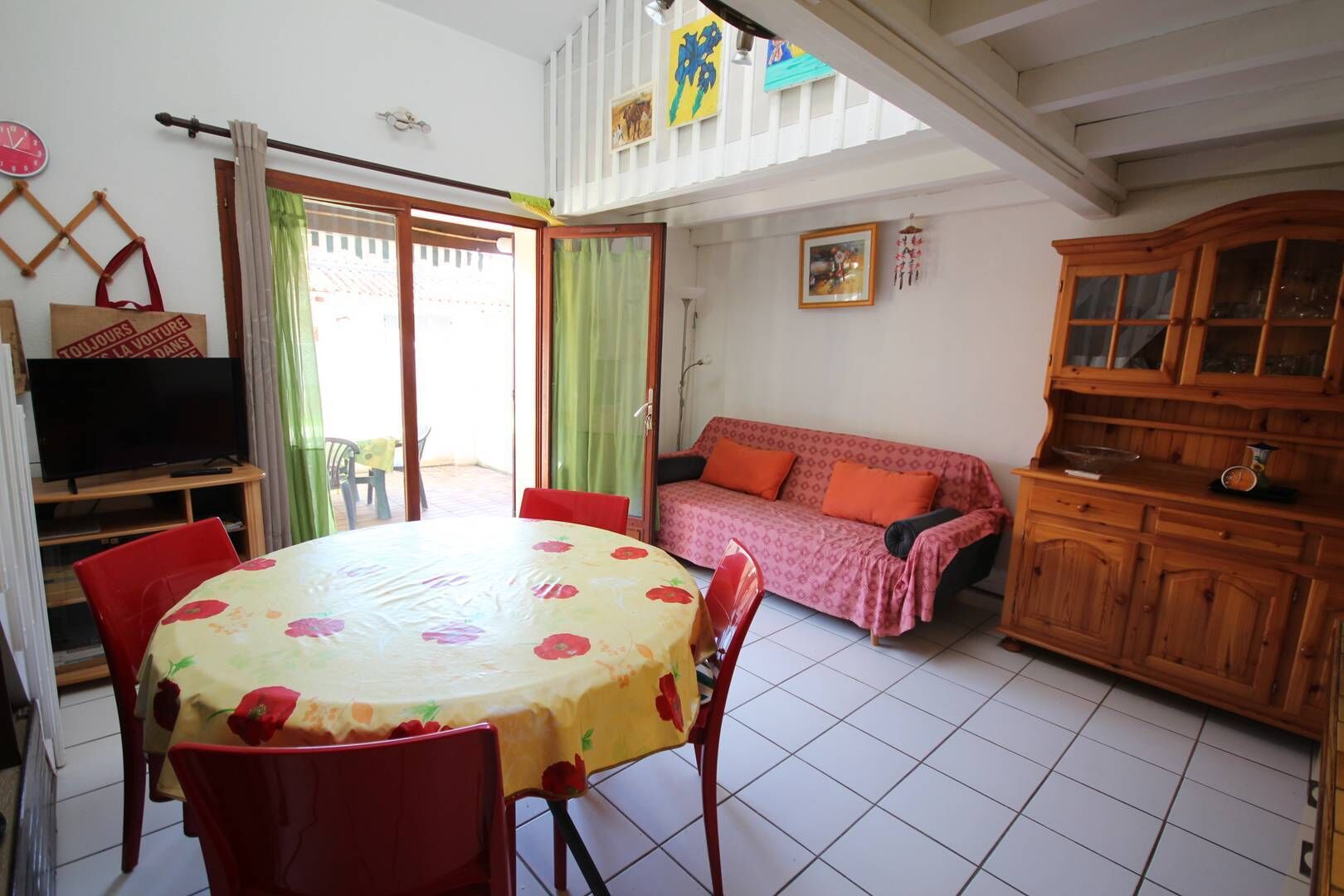 A cozy living room with a dining table, red chairs, a sofa, and a wooden cabinet.