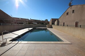 A swimming pool with a metal ladder, surrounded by a tiled deck and a low wall.