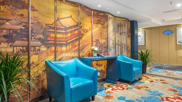 A reception area with traditional Chinese wall art, two blue armchairs, a desk with a vase, and a patterned carpet.