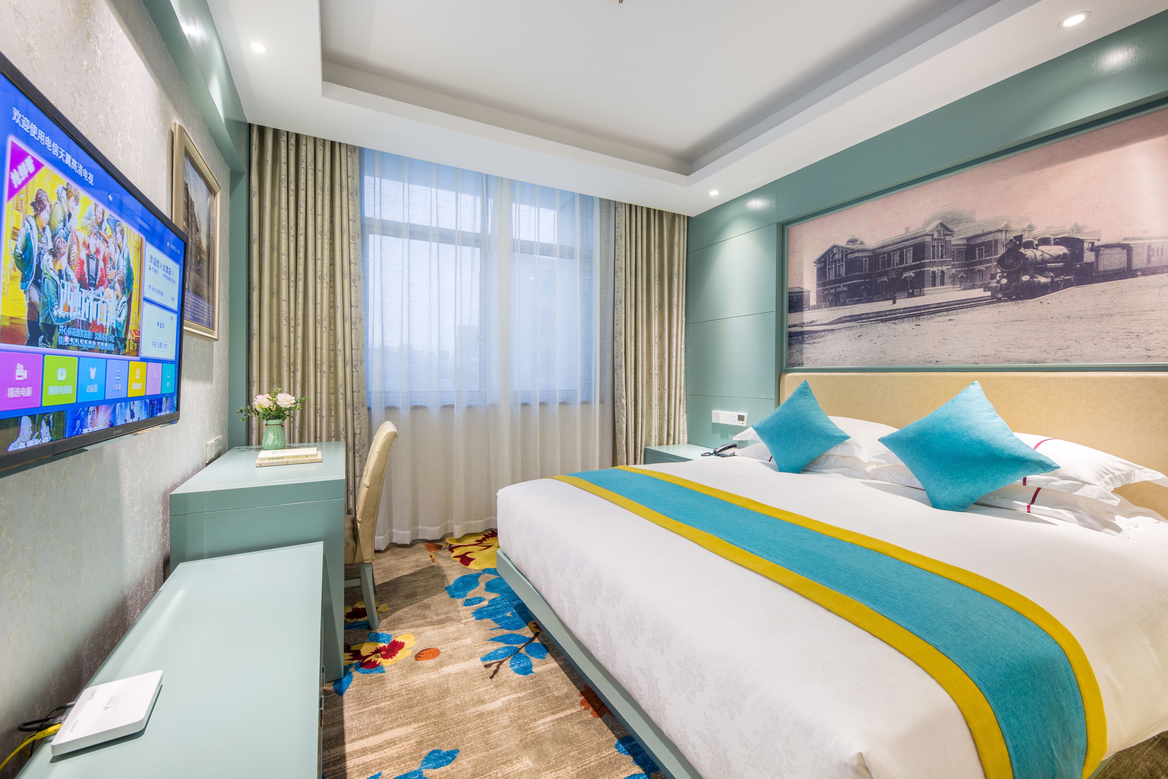 Quarto de hotel com uma cama grande, uma escrivaninha, televisão e janela com cortinas.