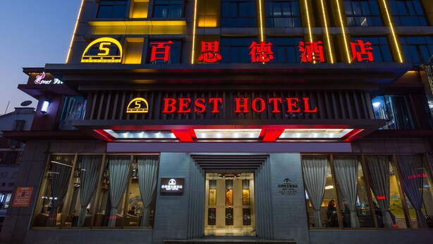 Un hotel con un llamativo letrero que dice 'BEST HOTEL' y un gran logotipo iluminado con una 'S'.