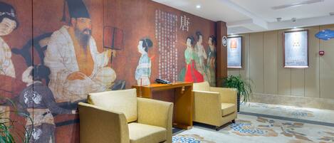 A lobby with traditional artwork, two armchairs, a wooden desk, and a patterned carpet.
