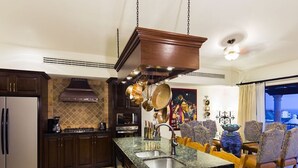 A kitchen with dark wood cabinets, a granite countertop, and a hanging pot rack. - Stunning 3 BR Villa at Hacienda Encantada in Cabo!  New Years Week!
Sleeps 10! (Cabo San Lucas)