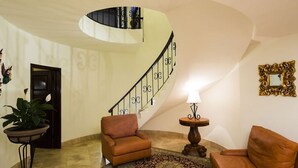 A spacious living area with a curved staircase, leather armchairs, a patterned rug, and a small table with a lamp. - Stunning 3 BR Villa at Hacienda Encantada in Cabo!  New Years Week!
Sleeps 10! (Cabo San Lucas)