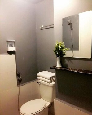 A bathroom with a toilet, a shower, a towel rack, and a small potted plant. - Lime Condo Rentals (Mandaluyong)