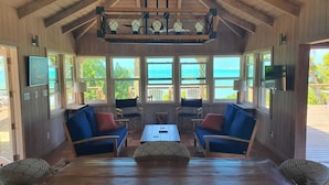 A cozy room with wooden walls and a wooden ceiling, featuring a large window with a view of the sea, two blue sofas, a wooden coffee table, and a television on the wall. - North Star - A completely secluded home - the quintessential beach bungalow (Elbow Cay)