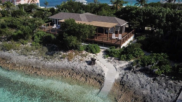 A beachfront property with a wooden deck and lounge chairs, surrounded by lush greenery and a clear view of the ocean. - North Star - A completely secluded home - the quintessential beach bungalow (Elbow Cay)