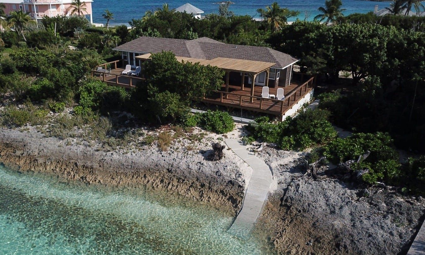 Ein Hotel direkt am Strand mit einer Holzterrasse und Liegestühlen, umgeben von üppiger Vegetation und freiem Blick auf den Ozean.