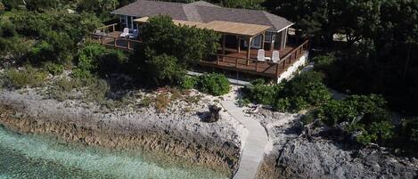 Ein Hotel direkt am Strand mit einer Holzterrasse und Liegestühlen, umgeben von üppiger Vegetation und freiem Blick auf den Ozean.