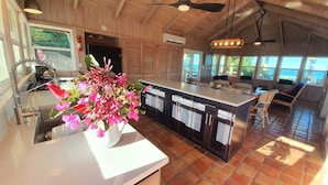 A modern kitchen with a central island, a dining area with chairs, and a view of the sea through large windows. - North Star - A completely secluded home - the quintessential beach bungalow (Elbow Cay)