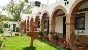 A courtyard with a fountain, potted plants, and a building with arched doorways. - Hospederia Marques Casa Ramos (Villa de Leyva)