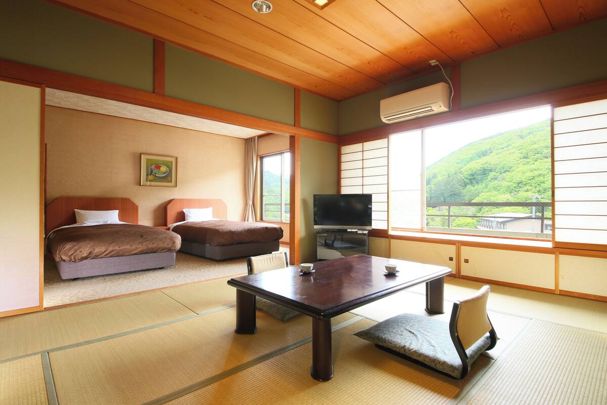 Um quarto em estilo japonês tradicional com tatames, uma mesa baixa, um sofá e uma televisão.