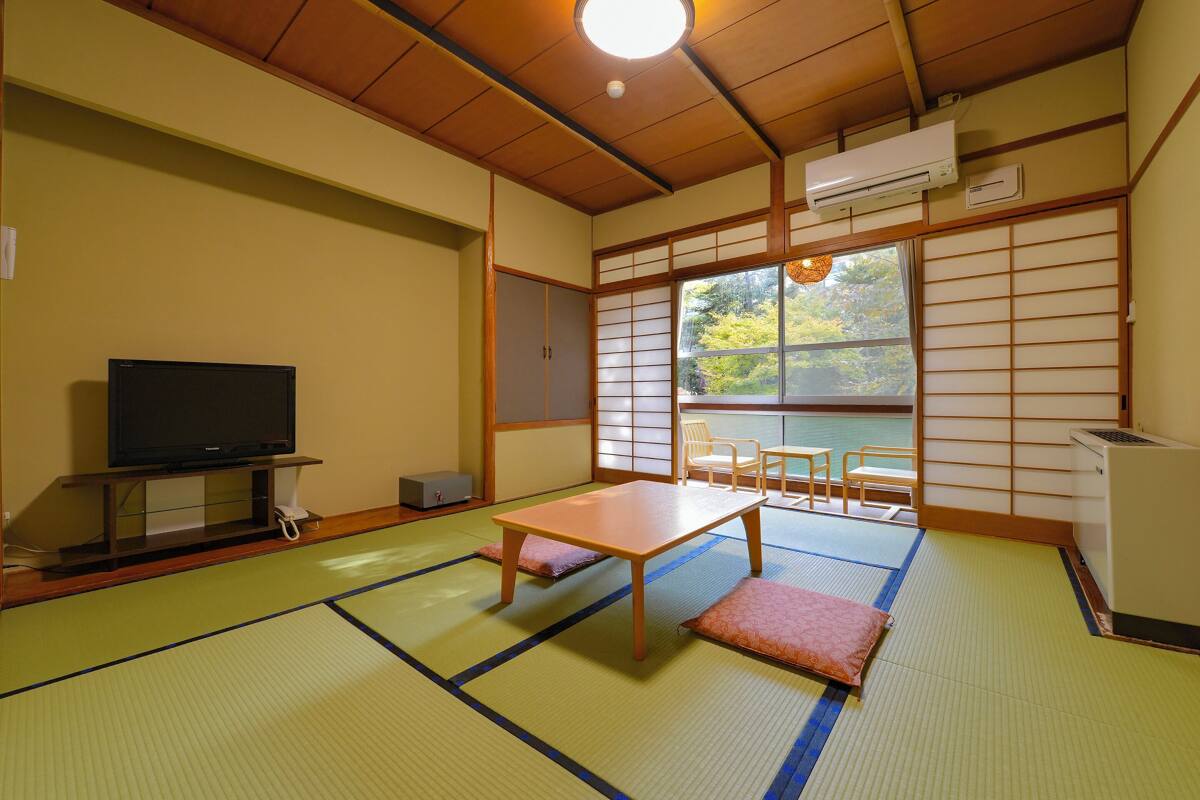 Quarto japonês tradicional com tatames, televisão, mesa e vista através de um shoji.