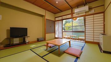 A traditional Japanese room with tatami flooring, a television, a table, and a view through a shoji screen.