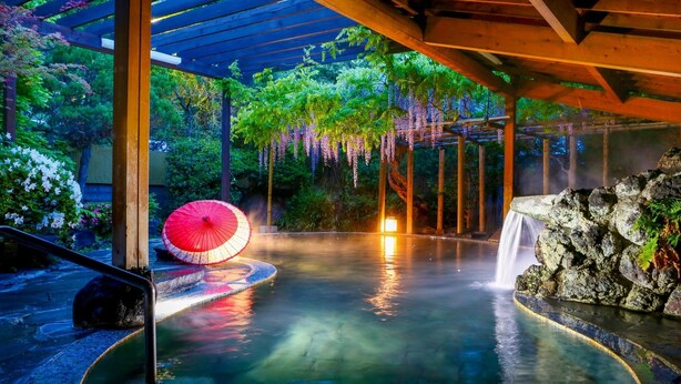 Een bronnenlandschap met een houten pergola, een rode parasol en een waterval.