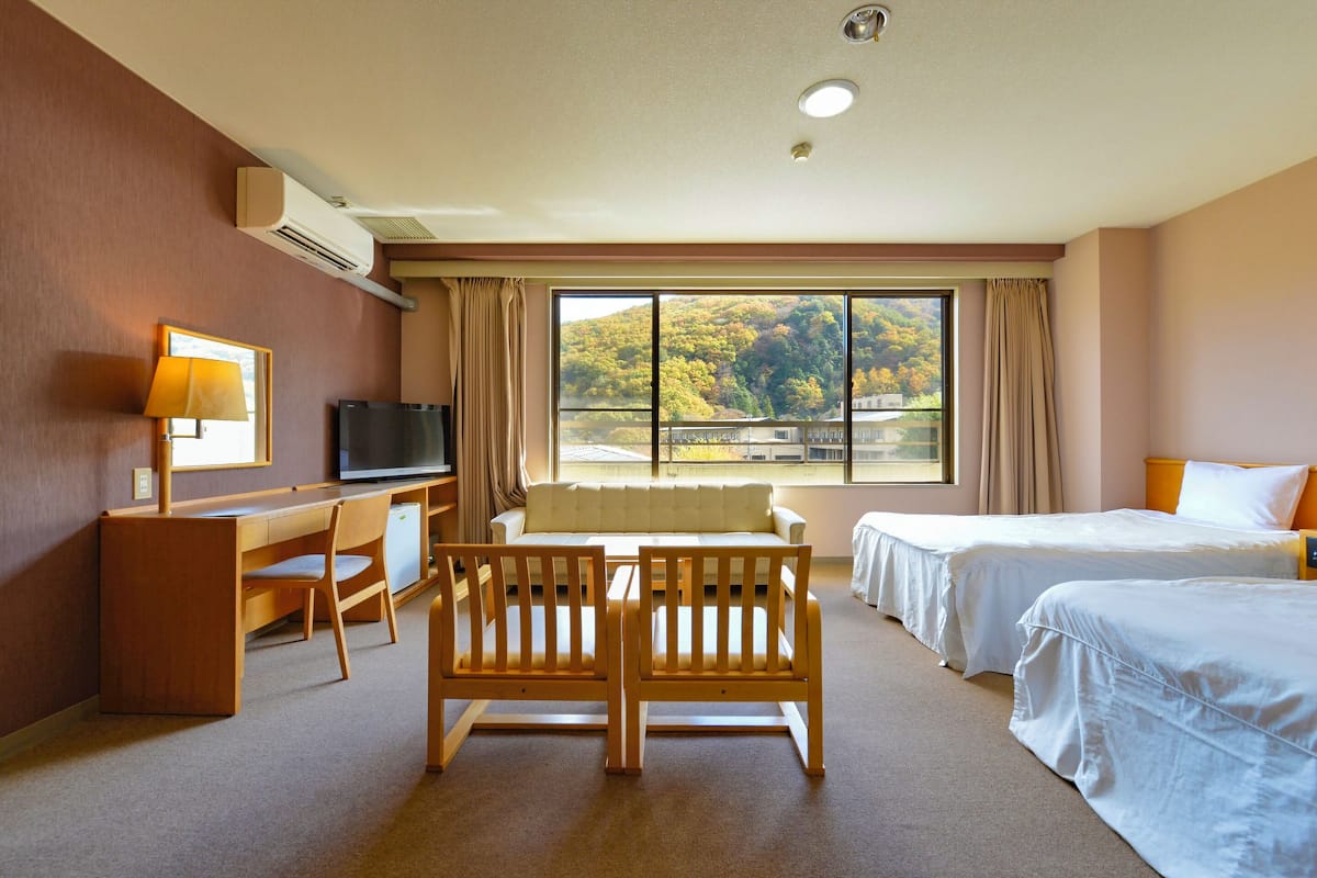 Quarto de hotel com escrivaninha, duas camas de solteiro, um sofá e uma televisão.
