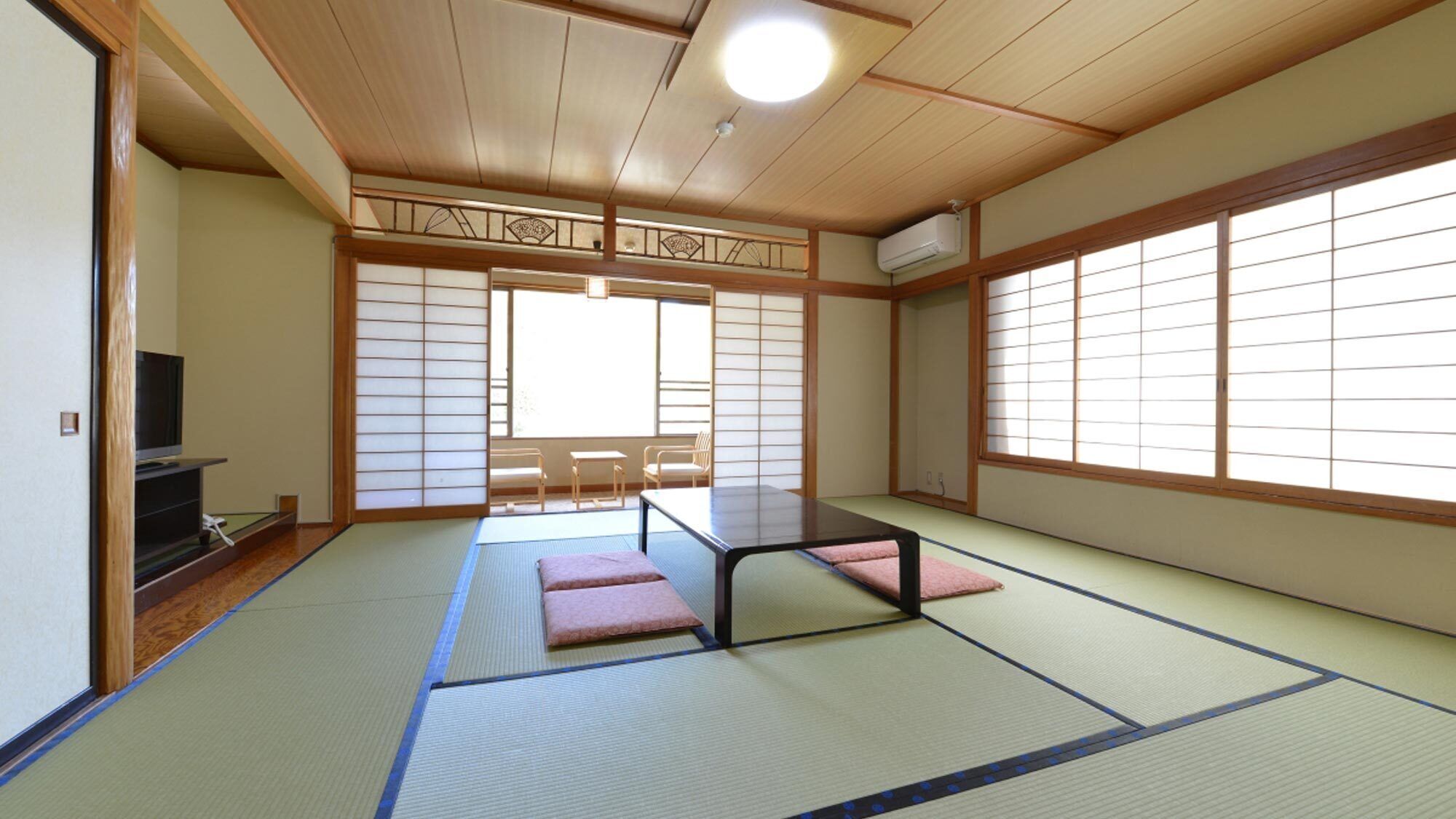 Una habitación japonesa tradicional con suelo de tatami, una mesa baja, cojines, puertas correderas y un televisor.