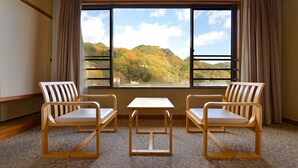 Een kamer met twee houten stoelen en een klein tafeltje, een groot raam met uitzicht op een bebost glooiend landschap.