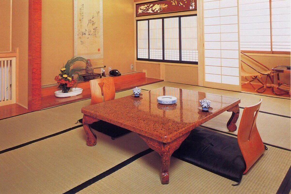 Ein traditioneller japanischer Raum mit Tatami-Bodenbelag, einem niedrigen Holztisch und einer Schiebetür mit dekorativem Bildschirm.