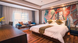 Ein Hotelzimmer mit einem großen Bett, einem Schreibtisch und einem Stuhl. Ein Fenster mit Vorhängen und ein Bild an der Wand sind ebenfalls vorhanden.
