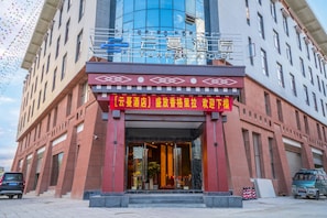 A hotel entrance with a red and white sign, glass doors, and a blue sky with colorful flags in the background.